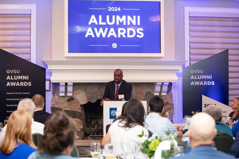 Quincy Williams speaking in microphone with 2024 Alumni Awards sign behind him